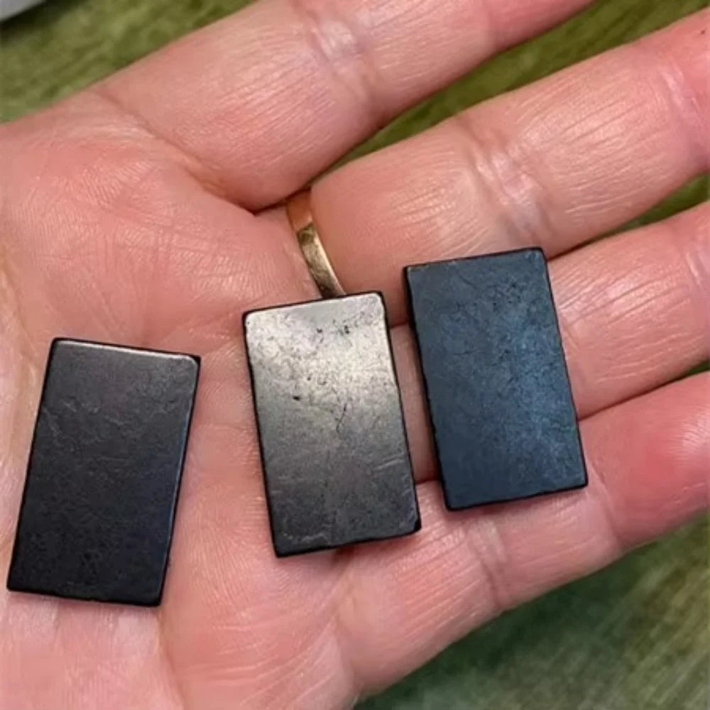 Three rectangular metal samples held in a hand with a green background