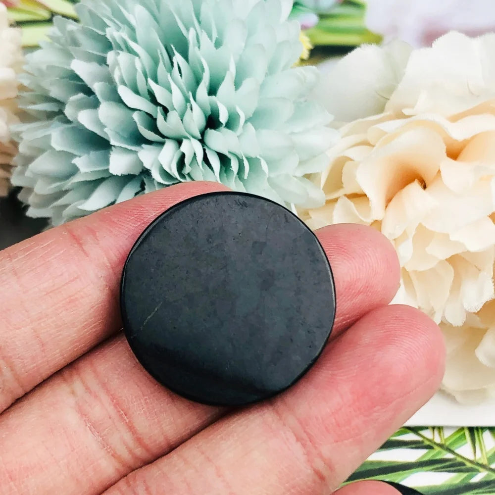 Black round object held between fingers with flowers in the background