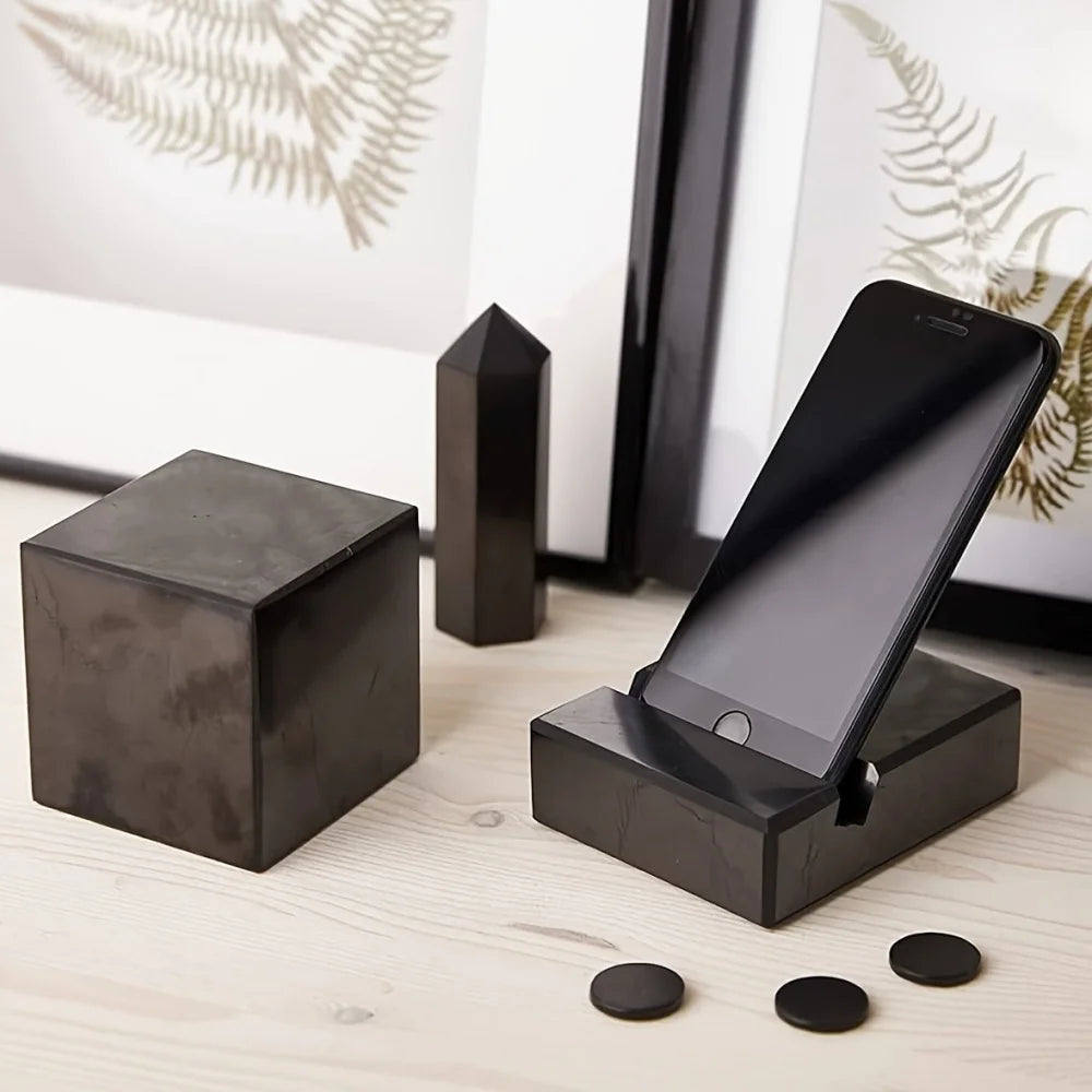Black stone-like phone stand with a smartphone on a light wooden surface.