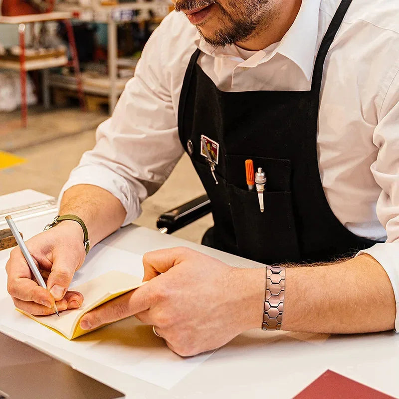 Person wearing a black apron writing in a notebook with a workshop in the background