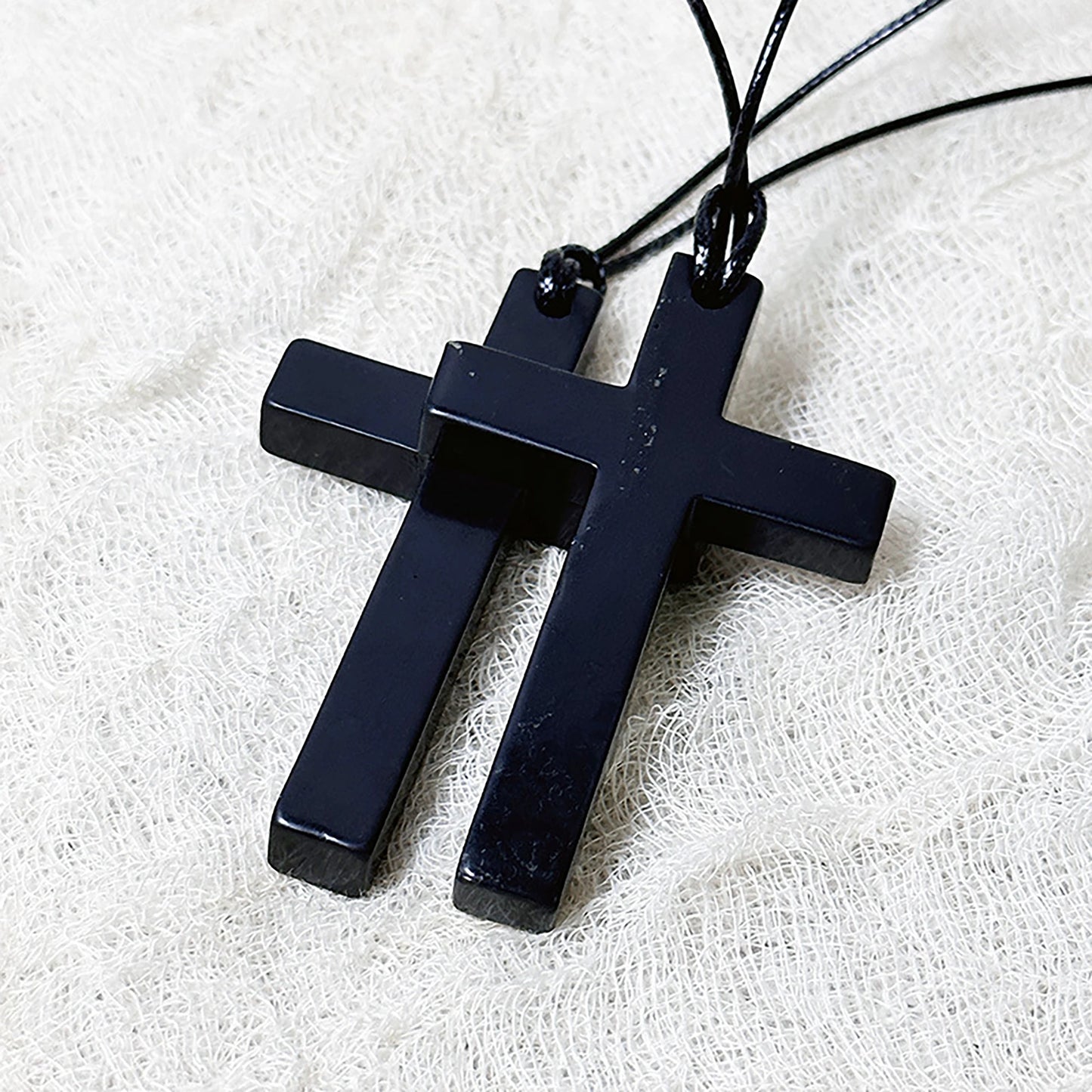 Black cross pendant necklace on a white fabric background
