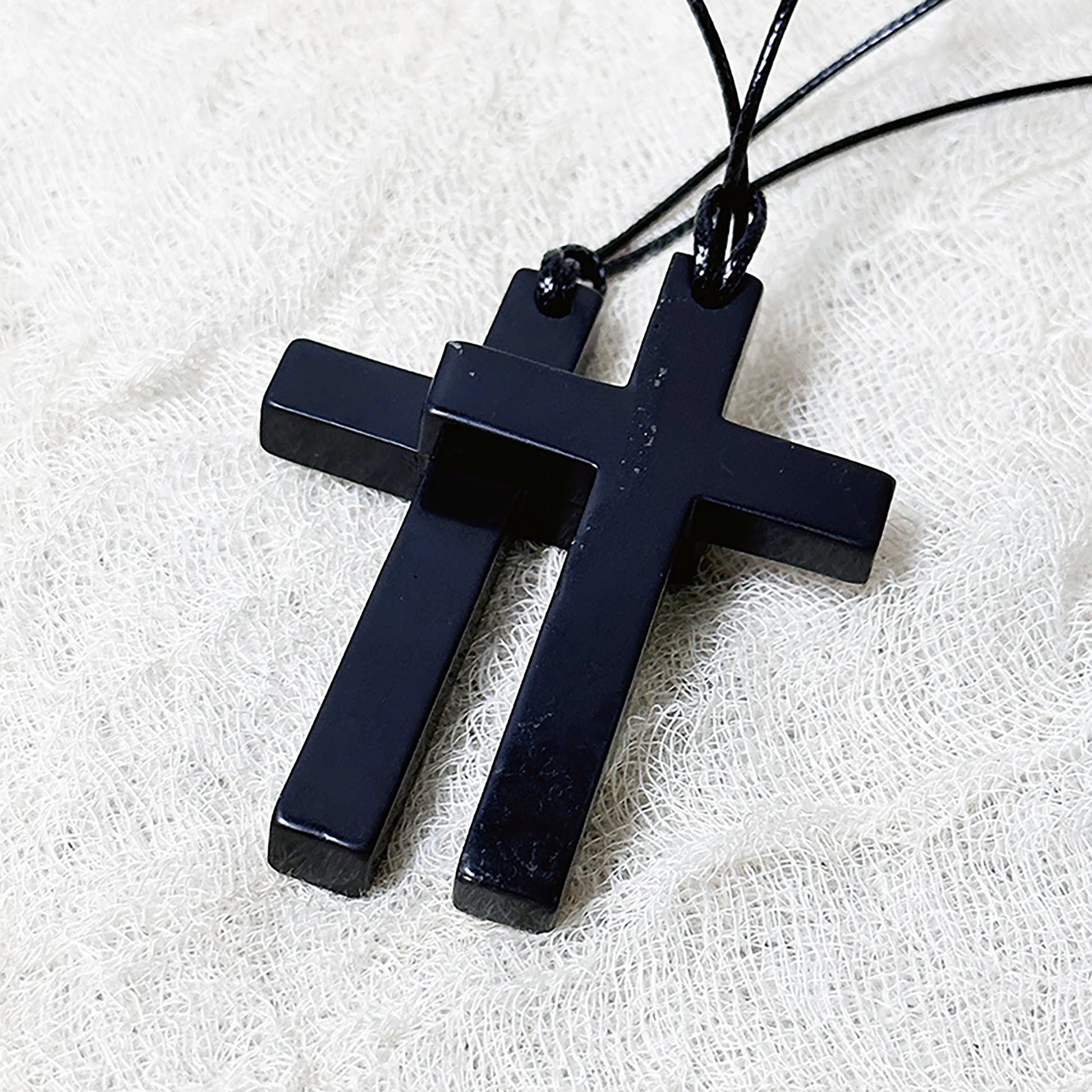 Black cross pendant necklace on a white fabric background