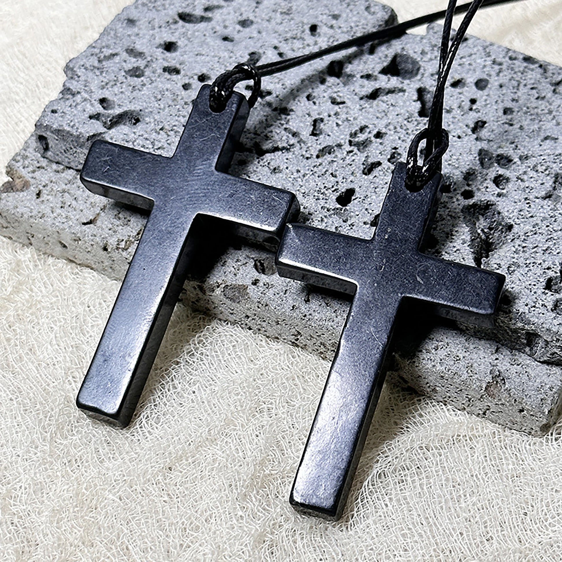 Two black cross-shaped pendants on a stone surface