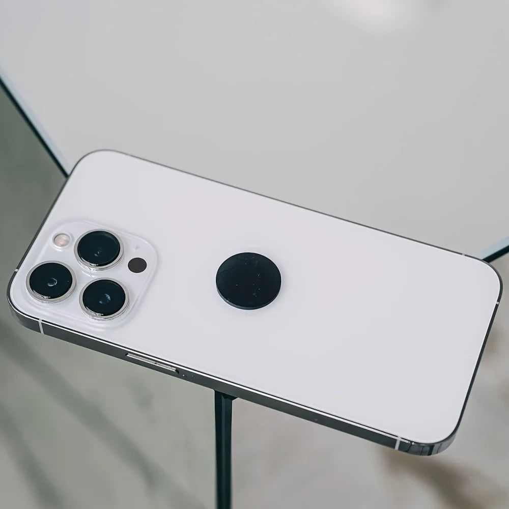 Smartphone with a white back and a black camera module on a reflective surface.with Shungite Phone Patch