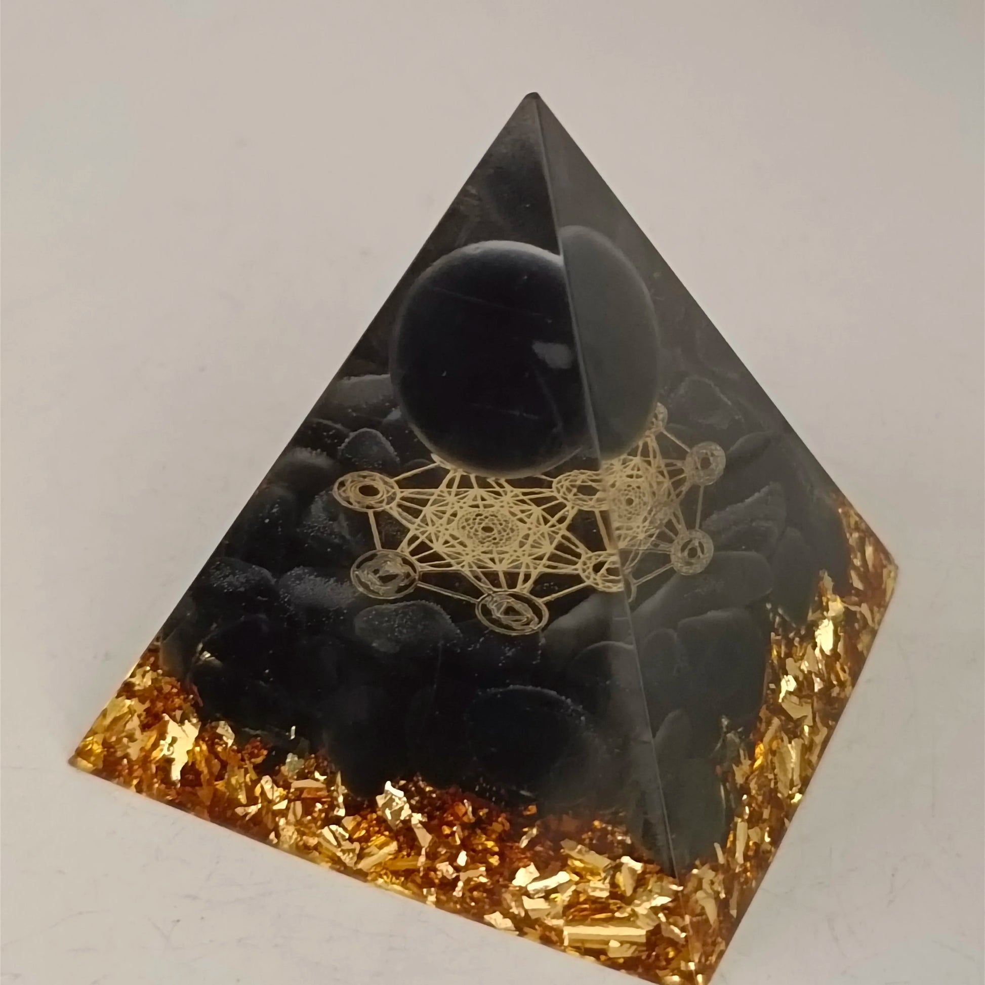 Pyramid-shaped object with black sphere and gold geometric design on a white background