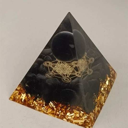Pyramid-shaped object with black sphere and gold geometric design on a white background